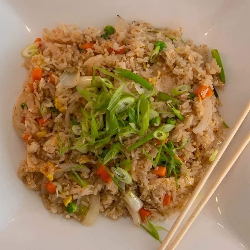 A white plate of fried rice with carrots, peas, and green onions, with chopsticks on the side.
