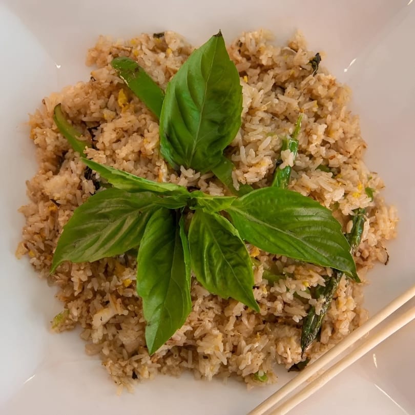 Thai basil fried rice with green beans and fresh basil leaves, served with chopsticks.