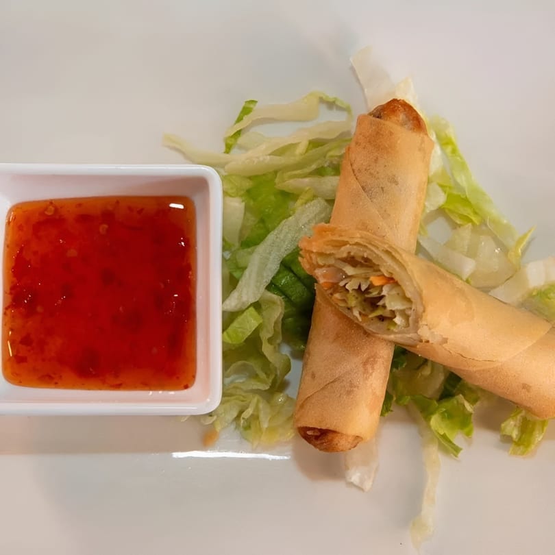 Two crispy spring rolls with sweet chili sauce and shredded lettuce on a white plate.