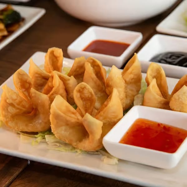 Crispy crab rangoons arranged on a white rectangular plate with two dipping sauces.
