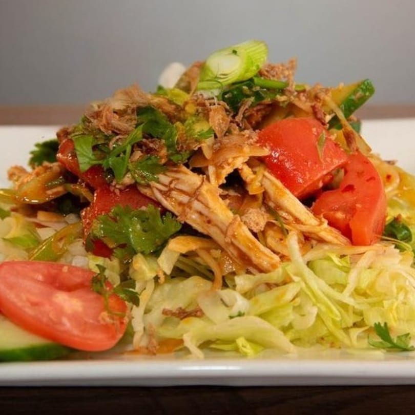 Shredded chicken salad with lettuce, tomatoes, cucumbers, and green onions on a white plate.