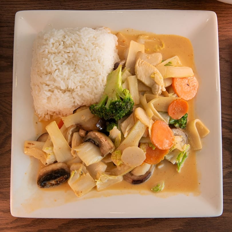 White plate with a serving of white rice and a yellow curry with chicken and vegetables.